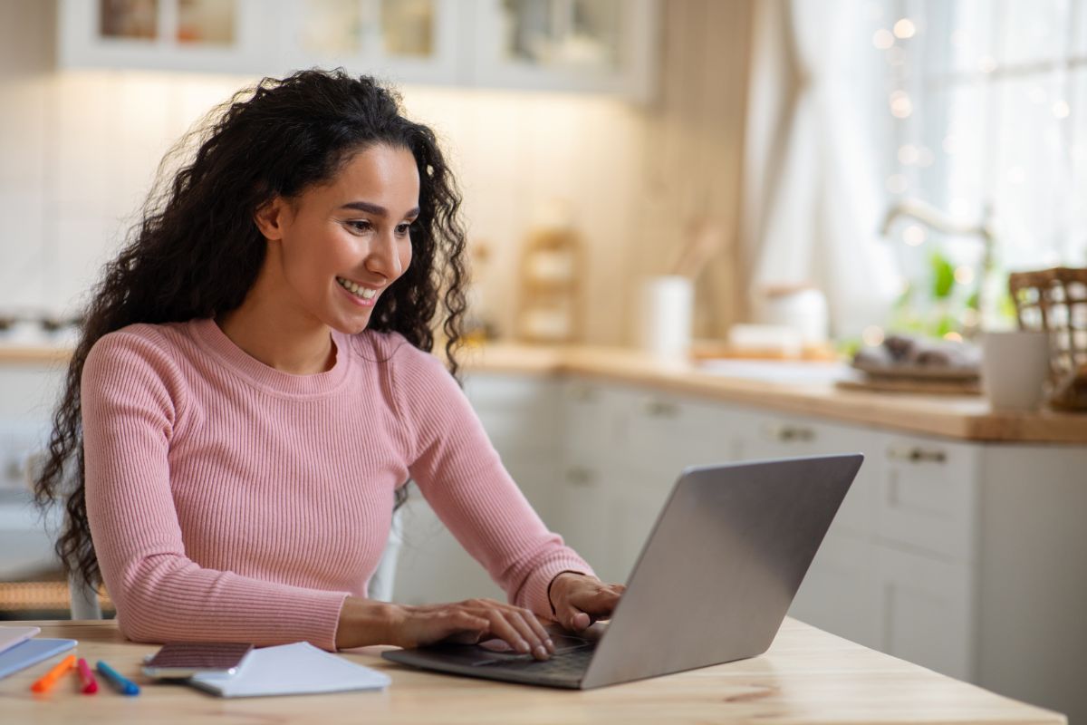 curly haired woman working on a laptop in the kitchen