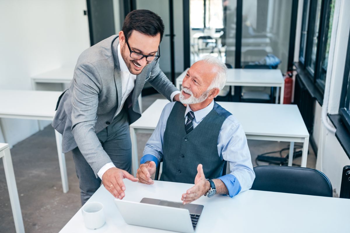 young gentle man in a suit helping older gentle man in a suit with technical skills
