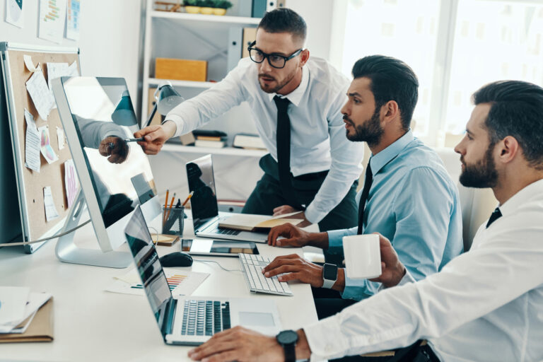 Group of young modern men in formalwear working using computers while sitting in the office