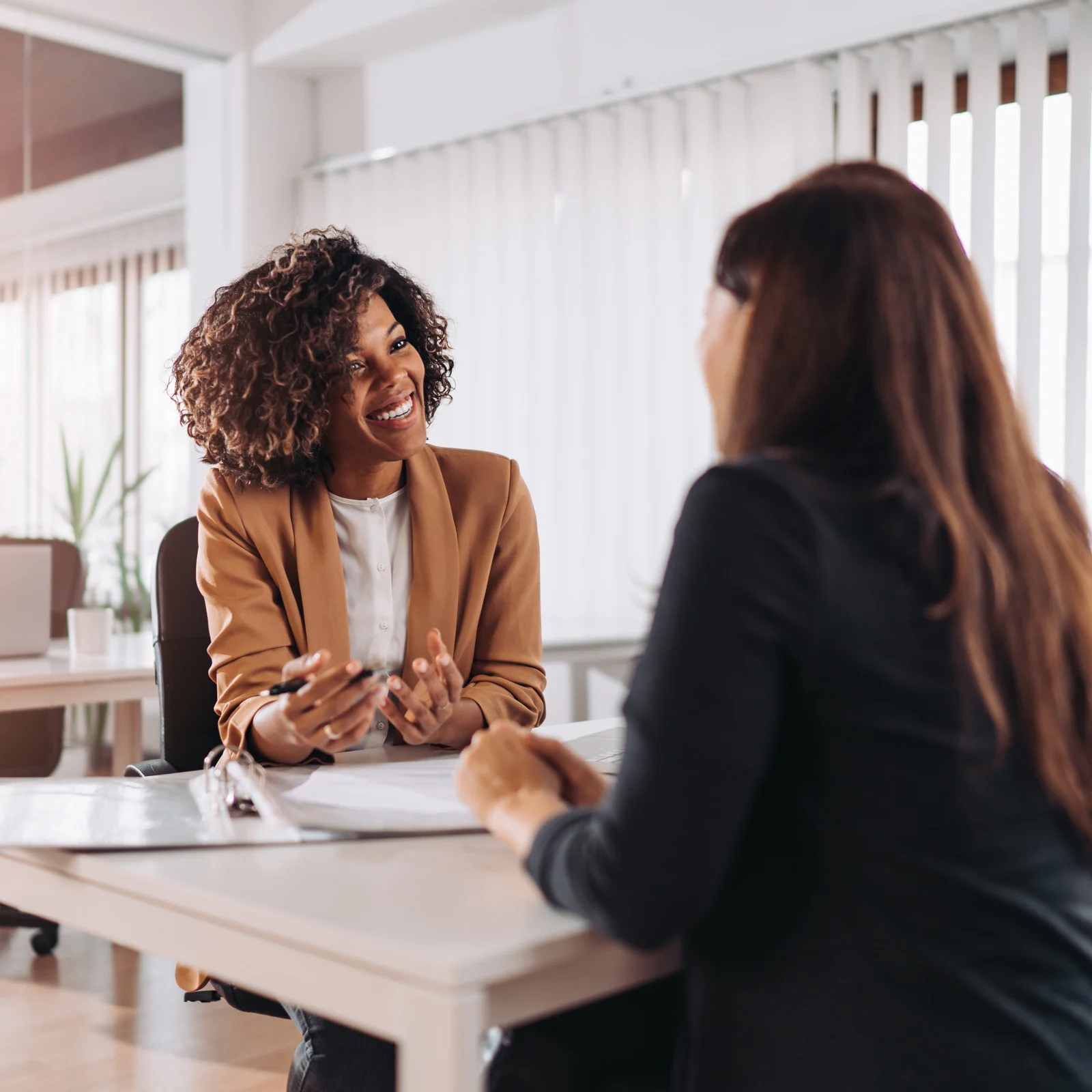 dark skinned woman in a brown blazer talking to a woman from across the table