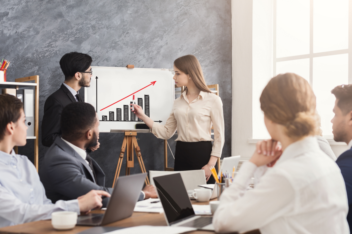 Man and woman leading a meeting with a white board showing an upward graph showcasing the growth of the company